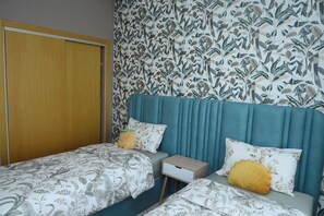 A bedroom with two beds, a wooden wardrobe, and a floral wallpaper. - Luxurious apartment with waterfront pool (Sidi Rahal Chatai)