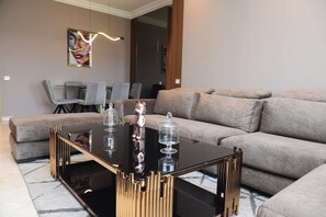 Un salon moderne avec une table basse en verre noir, un canapé beige et une statuette d’ours décorative.