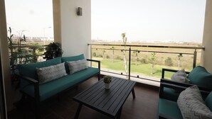Ein Balkon mit einer Couch und einem Tisch, Blick auf eine Rasenfläche und ein Gebäude in der Ferne.