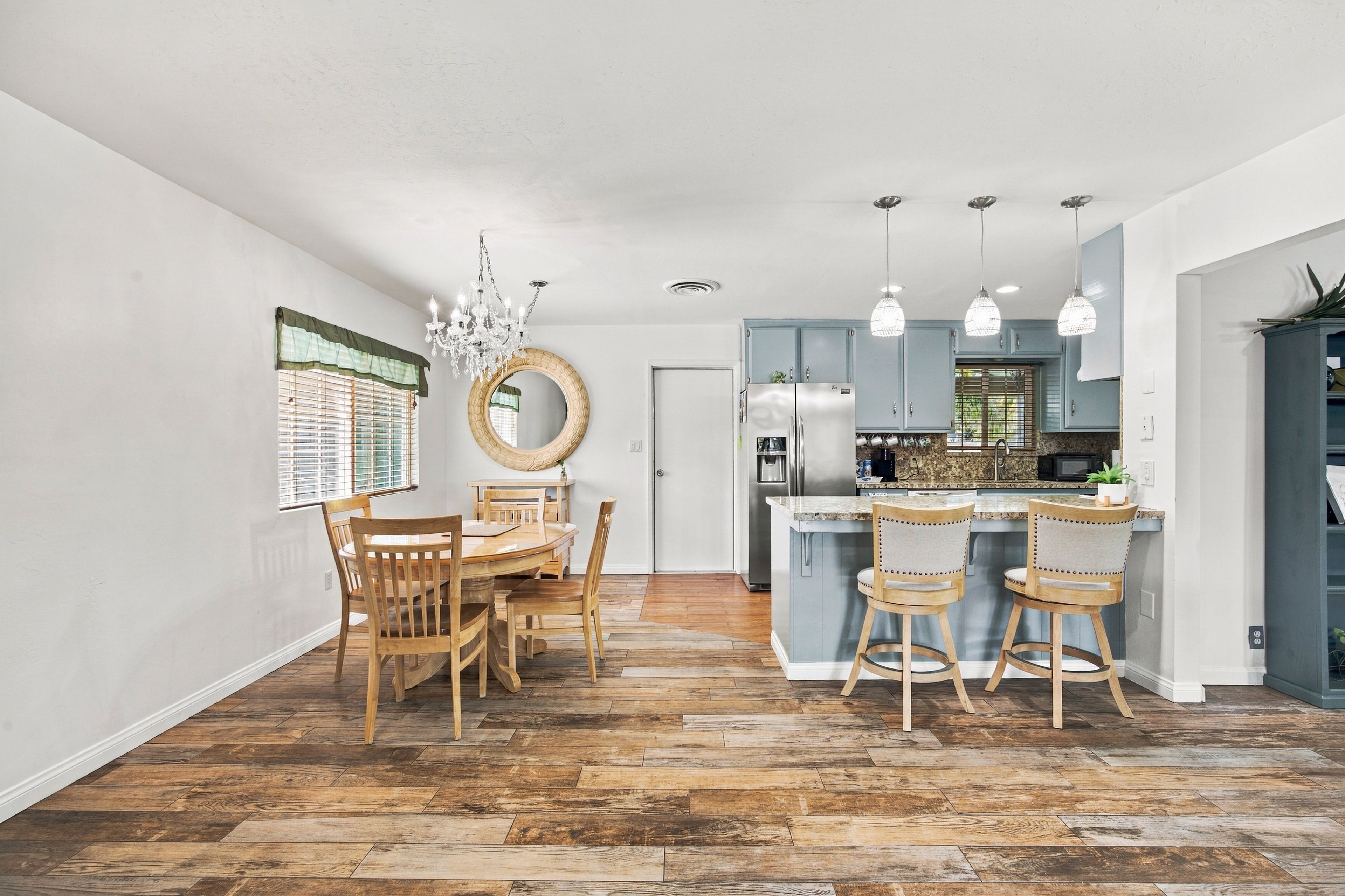 A spacious dining area with a wooden table and chairs, a chandelier, and a view into the kitchen.