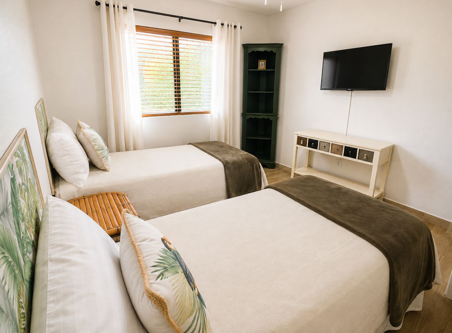 A hotel room with two beds, a television, a bookshelf, and a window with curtains.