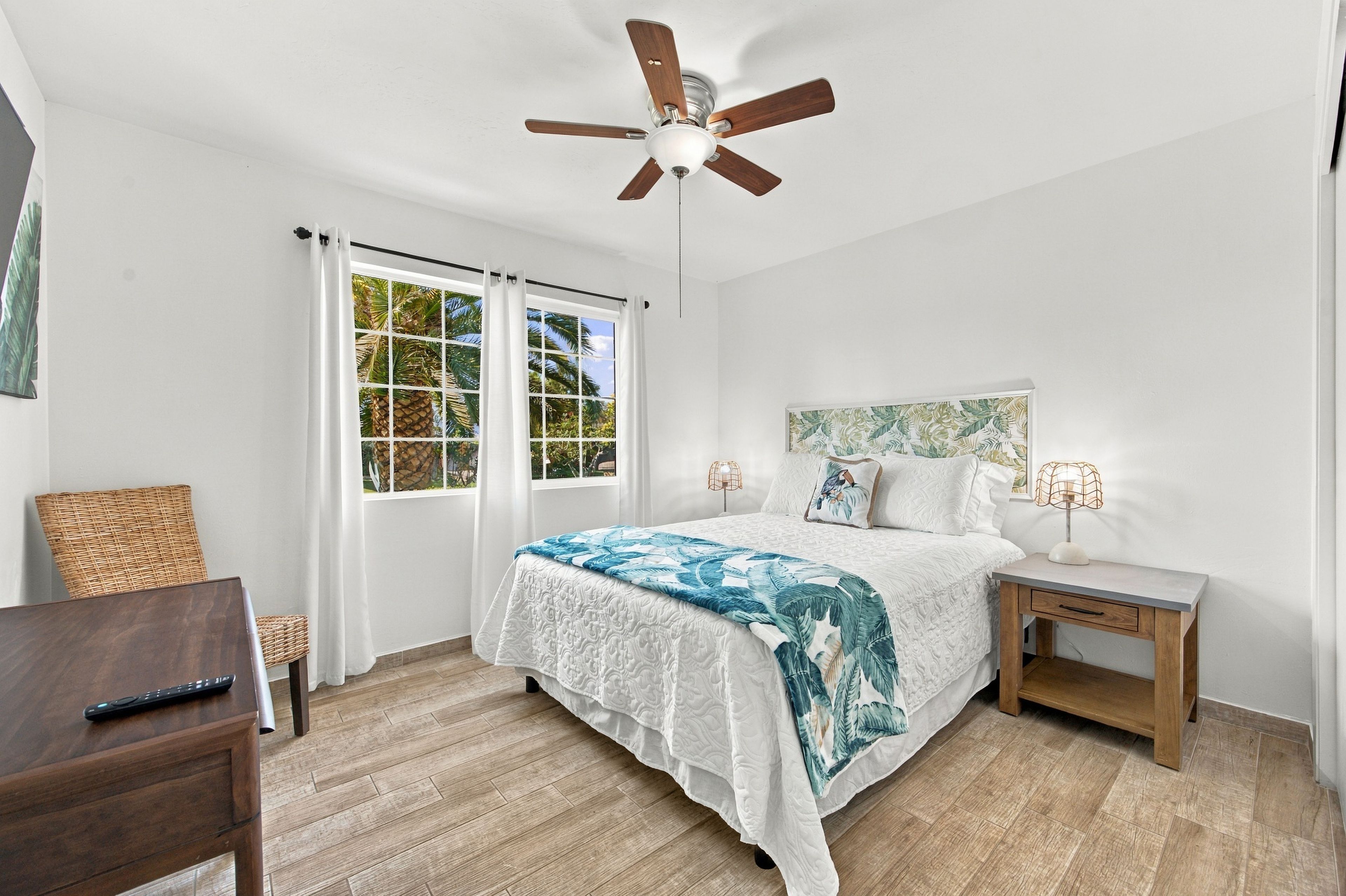 A bedroom with a bed, nightstands, a desk, a ceiling fan, and a window with curtains.