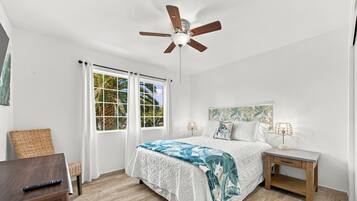 A bedroom with a bed, nightstands, a desk, a ceiling fan, and a window with curtains.