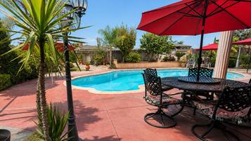 A pool area with a table and chairs, surrounded by palm trees and a red umbrella.