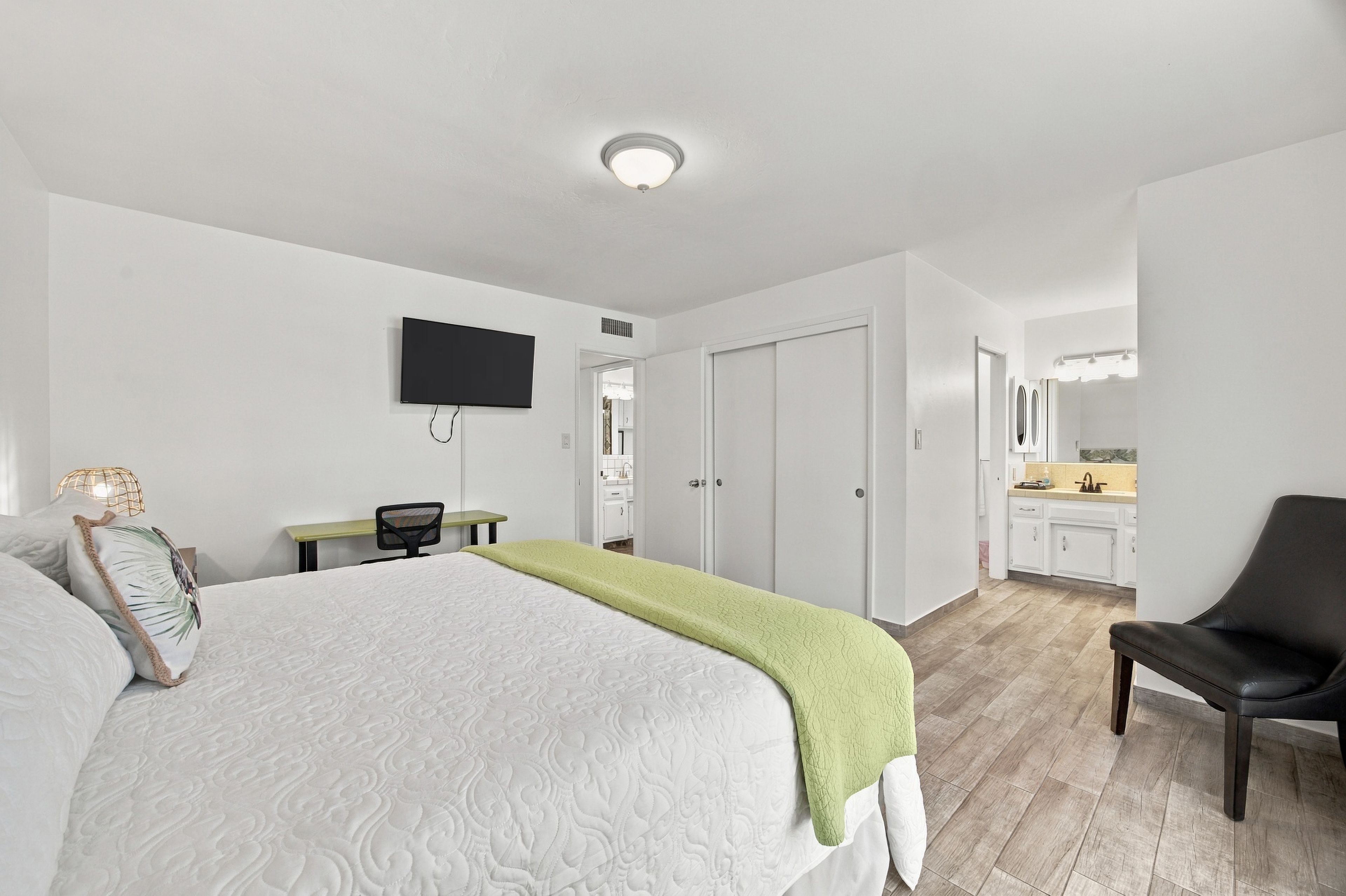A hotel room with a bed, a desk, a chair, a television, and a bathroom with a mirror.