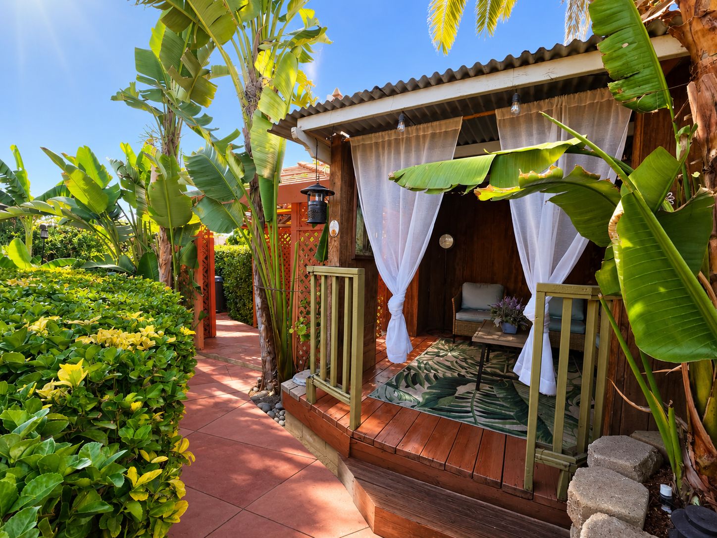 A tropical-style outdoor room with a wooden deck, a small table, and a chair.