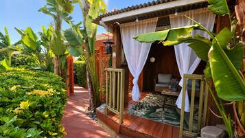 A tropical-style outdoor room with a wooden deck, a small table, and a chair.