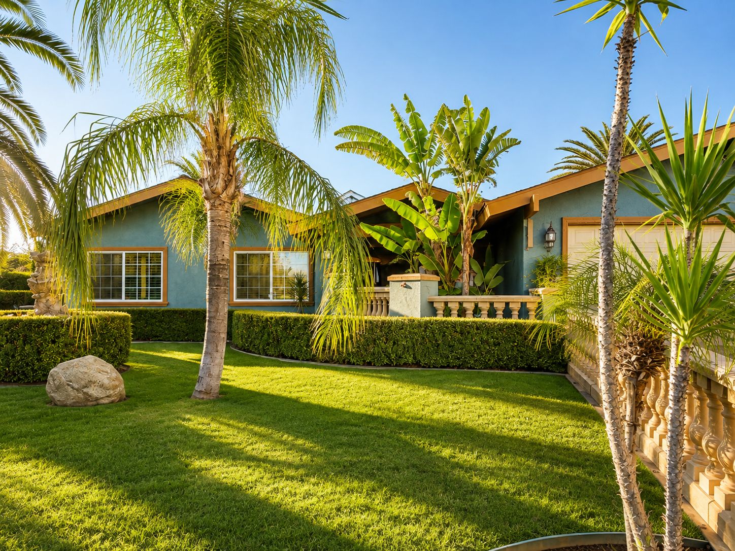 A residential property with a well-maintained lawn, palm trees, and a house with a light blue exterior and a brown roof.