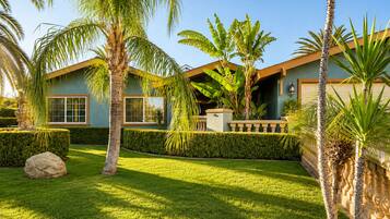 A residential property with a well-maintained lawn, palm trees, and a house with a light blue exterior and a brown roof.