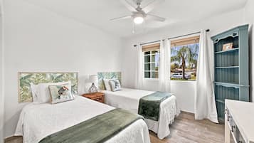 A bedroom with two beds, a ceiling fan, a window with curtains, and a wooden floor.