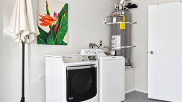 A laundry room with a front-loading washing machine and dryer, a water heater, and a painting of a flower on the wall.