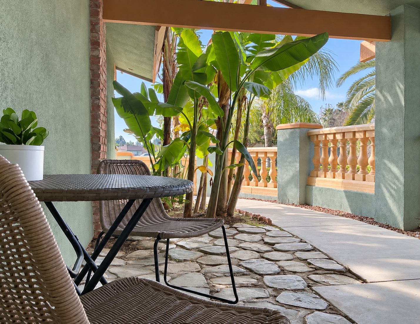 A covered outdoor seating area with wicker furniture and a potted plant.