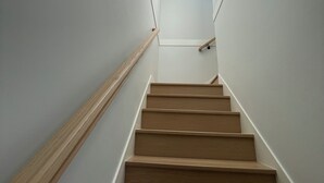Un escalier avec des marches en bois et des murs blancs, menant à un palier où se trouve un luminaire.