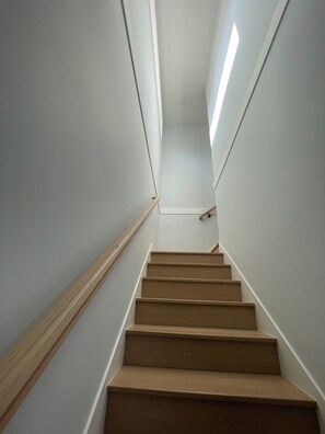 A staircase with wooden steps and white walls, leading to a landing with a light fixture.