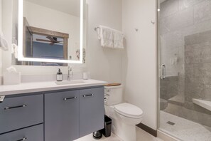 Et moderne badeværelse med brusekabine i glas, et hvidt toilet og en vaskebord med spejl og vask.
