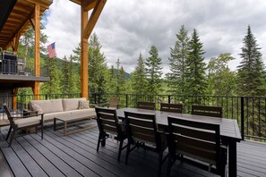 En træterrasse med sofa, spisebord og stole, med udsigt over et skovområde med et flag.