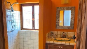 Een badkamer met een douche, wastafel, spiegel en raam.