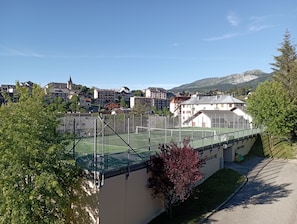 Ein Tennisplatz mit Zaun, umgeben von Gebäuden und Bäumen.