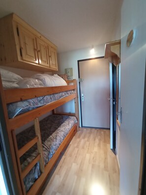 Ein Schlafraum mit Etagenbetten, Holzschränken, einer Tür und einem Lichtschalter an der Wand.