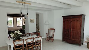 A dining area with a white table, wooden chairs, a rocking chair, and a wooden cabinet. - Mas in the middle of vineyards, ideally located between Camargue and Provence. (Vauvert)