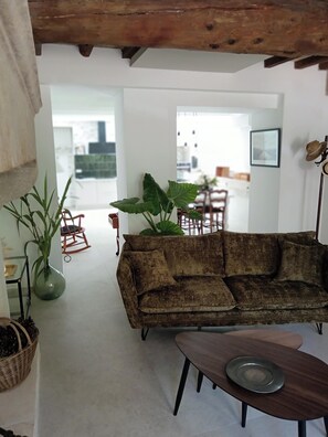 Una sala de estar con sofá, una mesa de centro, techo de madera, planta y una mecedora.