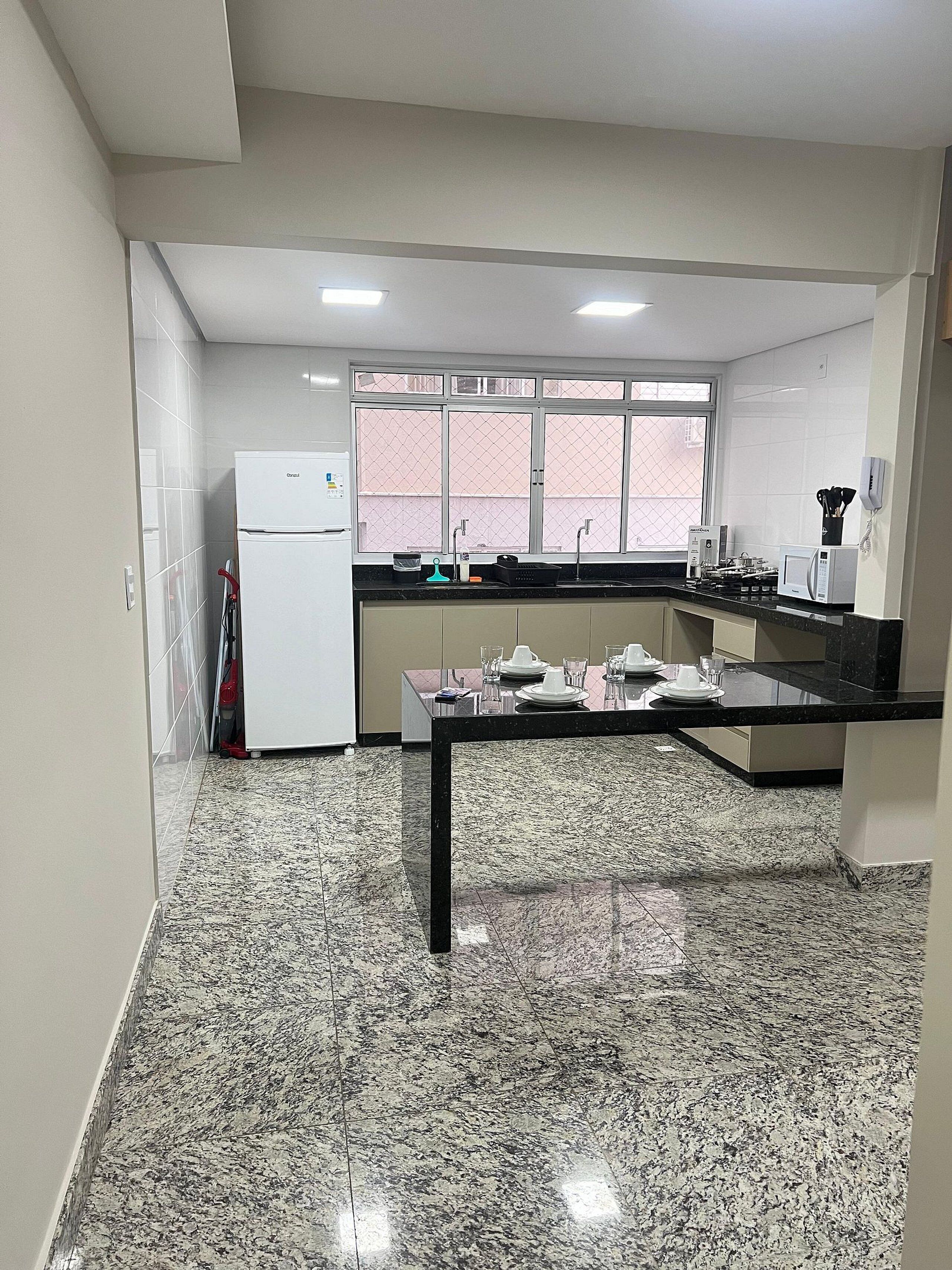 A kitchen with a refrigerator, microwave, sink, and granite countertop.