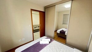 Une chambre d’hôtel avec un lit, un miroir, une porte donnant sur une autre pièce et un luminaire au plafond.