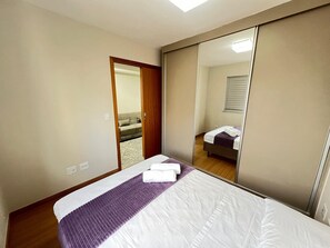 Ein Hotelzimmer mit Bett, Spiegel, einer Tür zu einem weiteren Raum und einer Deckenleuchte.