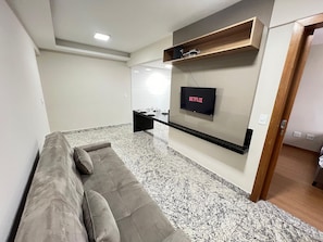A modern living room with a sofa, a flat-screen TV mounted on the wall, a wooden shelf, and a marble floor. - LK Santa Efigênia 3 (Belo Horizonte)