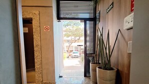Un couloir doté d’un sol en marbre, de plantes en pot, d’un panneau indiquant qu’il est interdit de fumer et offrant une vue sur la rue.