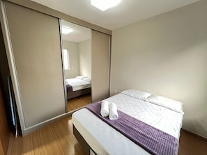 A bedroom with a bed, a mirror, a wardrobe, and a window. - LK Santa Efigênia 3 (Belo Horizonte)