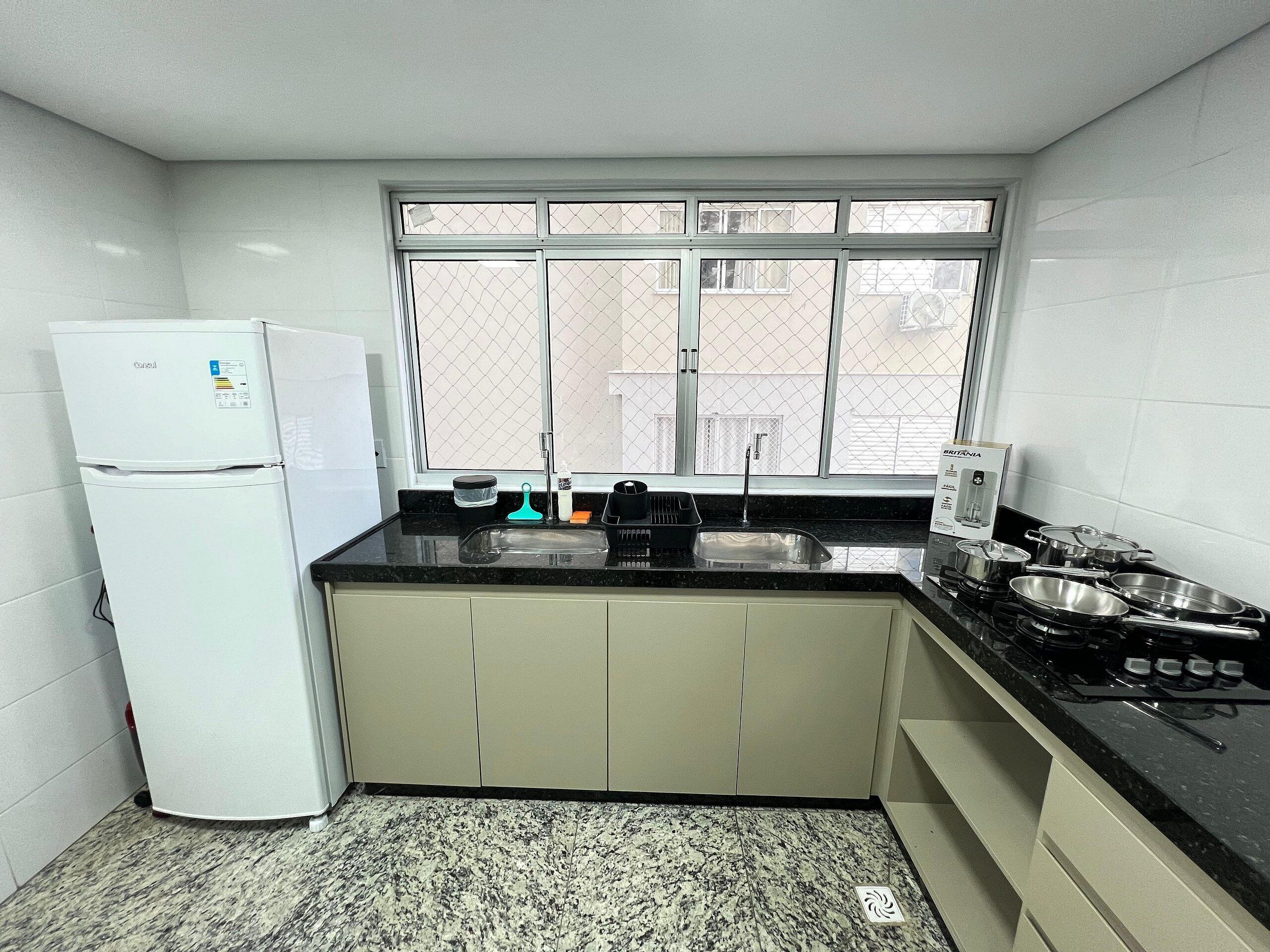 A compact kitchen with a refrigerator, sink, stove, and window.