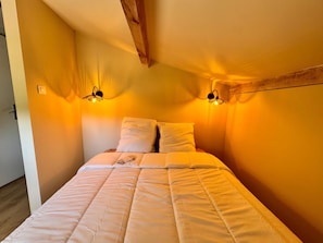 A bedroom with a bed, two wall-mounted lamps, and a wooden ceiling beam. - Vacation Home in the Alpilles, Provence (Noves)
