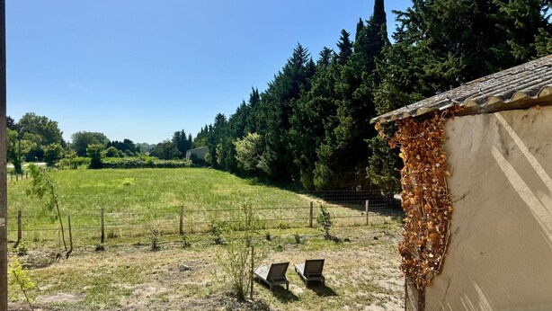 Paisatge rural amb un camp tancat per una tanca, un edifici petit amb teules i una banca de fusta.