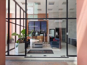 Een moderne hotelentree met grote glazen deuren, een receptiebalie, een zithoek en uitzicht op de stad.