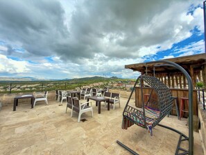 An outdoor seating area with tables and chairs, a hanging swing, and a view of the countryside. - Gülperi Cave Otel (Nevşehir)