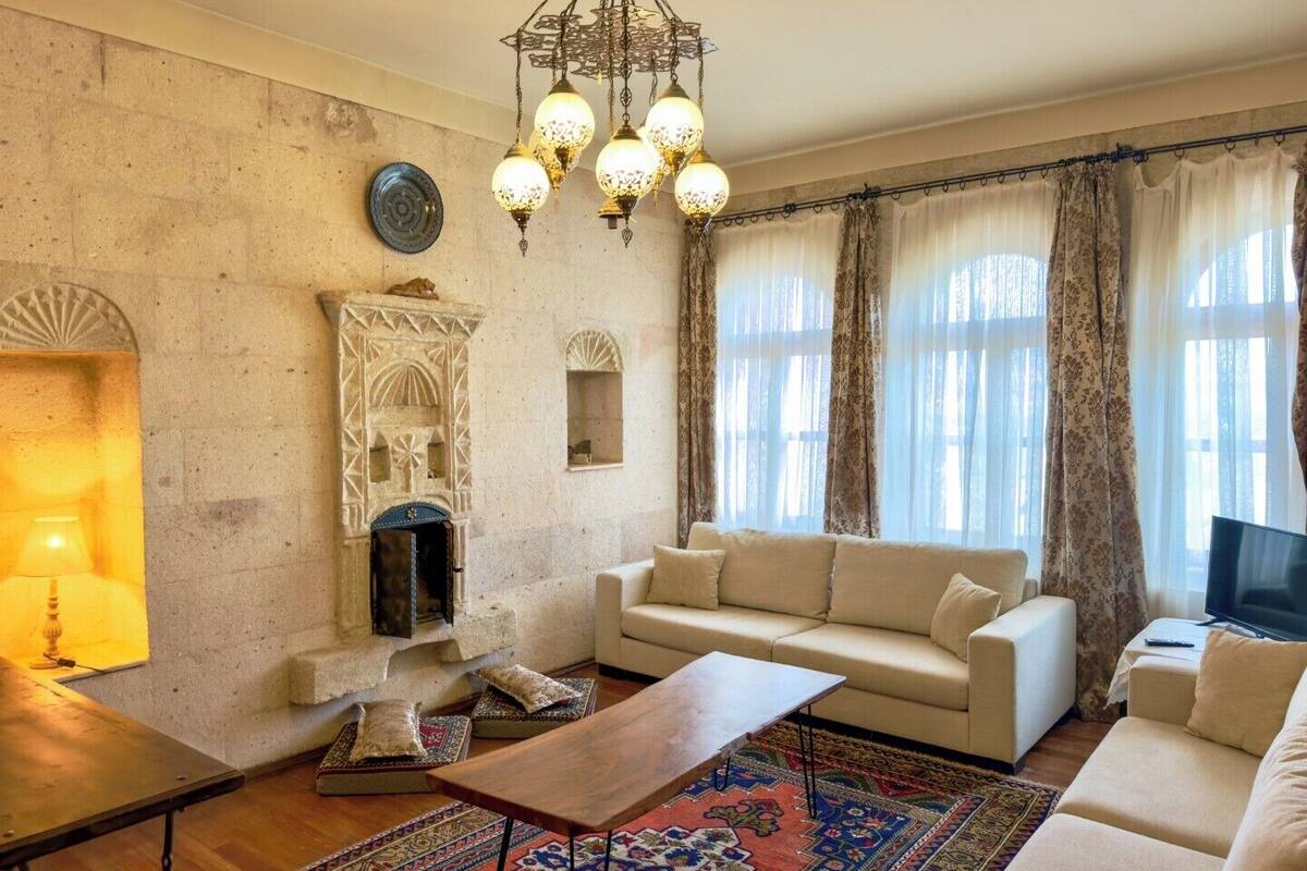 A living room with a sofa, a coffee table, a patterned rug, a fireplace, and a chandelier.