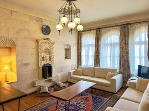 Ein Wohnzimmer mit einer Couch, einem Couchtisch, einem gemusterten Teppich, einem Kamin und einer Chandelier.