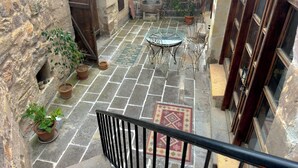 Ein Innenhof mit Steinfliesen, Blumentöpfen, einem Glastisch mit Metallstühlen und einem gemusterten Teppich.
