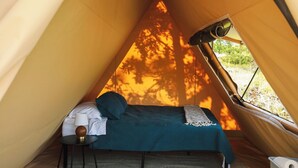 Une tente équipée d’un lit, d’une lampe et offrant une vue sur les arbres par la fenêtre.