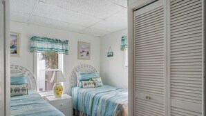 Een slaapkamer met twee bedden, een raam met jaloezieën, een nachtkastje en een deur.