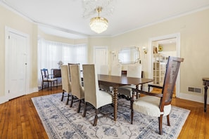 Une salle à manger avec une grande table, des chaises, un lustre et un tapis à motifs.