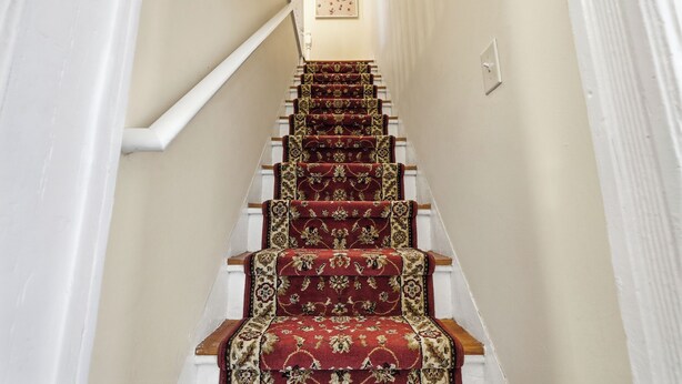 A staircase with red carpeted steps and white walls. - Spacious 9-bedroom house in perfect Asbury Park two blocks from the beach (Asbury Park)