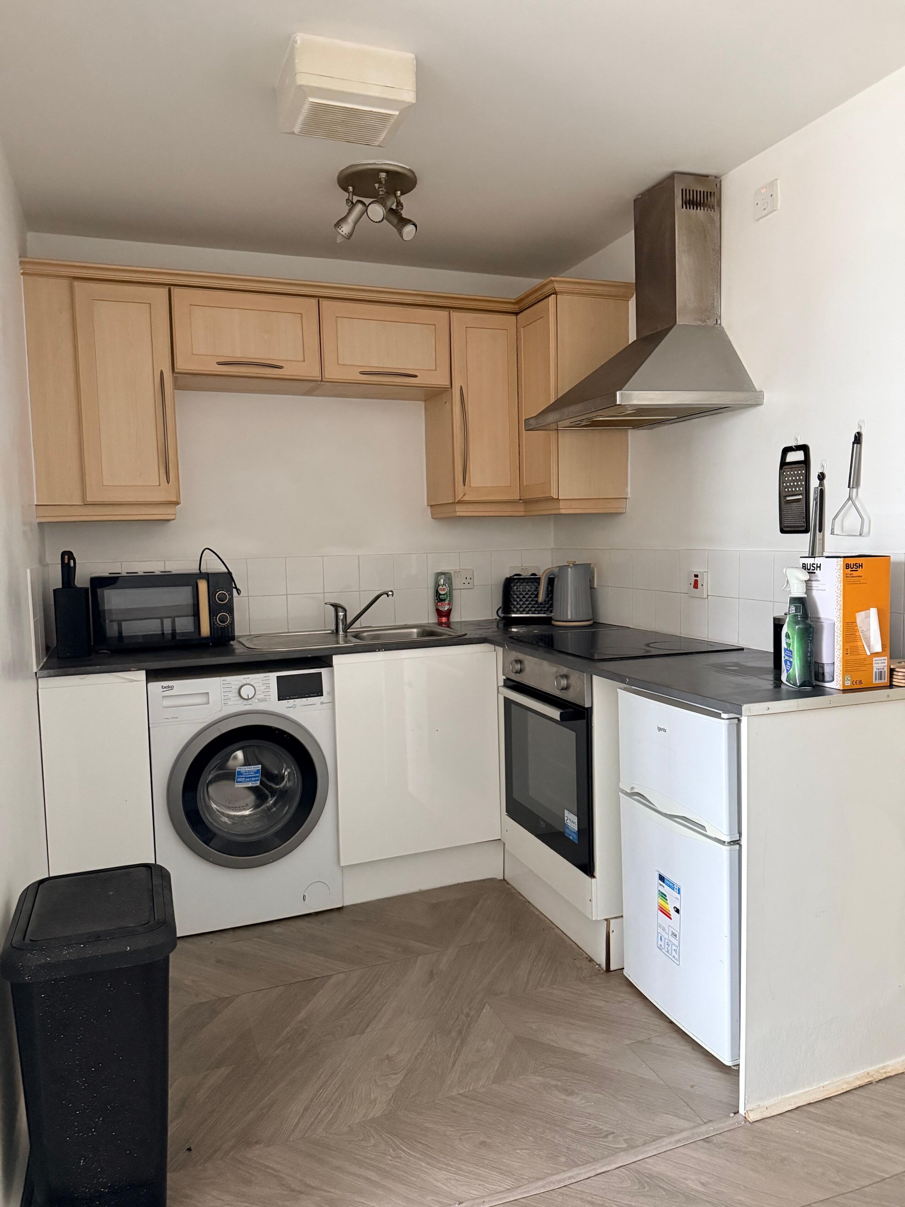 Une cuisine compacte dotée de meubles en bois, d’un lave-linge, d’un four à micro-ondes, d’une cuisinière et d’un réfrigérateur.