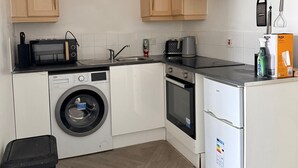 Ett kompakt kök med träskåp, tvättmaskin, mikrovågsugn, spis och kylskåp.