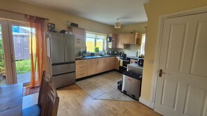 A compact kitchen with a refrigerator, stove, and sink, wooden cabinets, and a tiled floor. - Attractive 3-bedroom house in scenic Oranmore for your getaway (Oranmore)