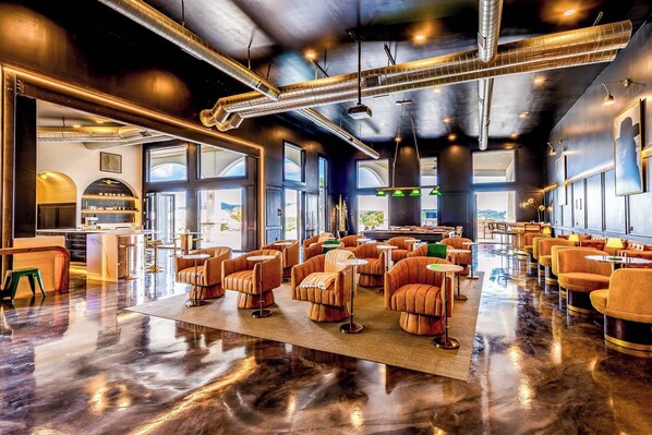 A spacious lounge area with modern seating, large windows, and visible kitchen area.