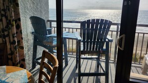 En balkong med två Adirondack-stolar, ett bord och utsikt över havet.
