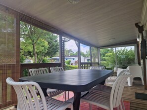 A covered outdoor area with a table and chairs, a wooden floor, and a view of houses and trees. - Mobile home in leisure residence (Saint-Gilles-Croix-de-Vie)