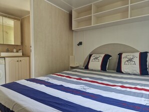 A bedroom with a bed, a wardrobe, a mirror, and a shelf unit. - Mobile home in leisure residence (Saint-Gilles-Croix-de-Vie)